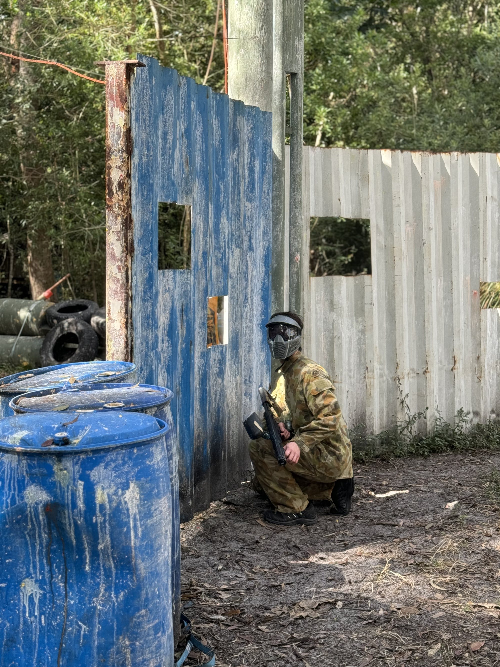 A paintball player taking cover behind painted barricades on the forest range at Twin Waters