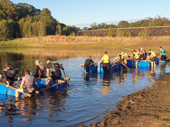 A team paddling their built raft out from the bank